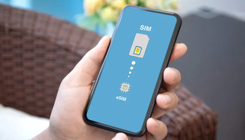 Dłoń trzyma smartfon z ekranem pokazującym ikonę karty SIM i chip eSIM, symbolizując przejście na technologię eSIM.