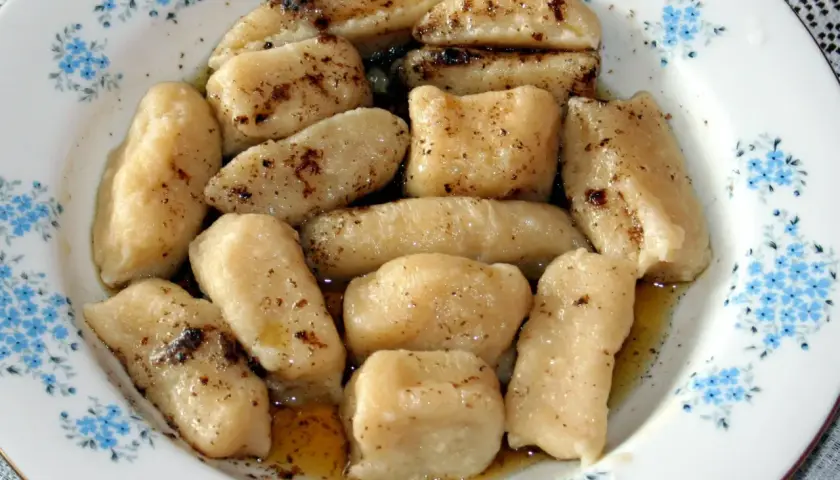 Gotowe pierogi leniwe, polane masłem i posypane cynamonem, czekają na talerzu z niebieskimi kwiatuszkami.