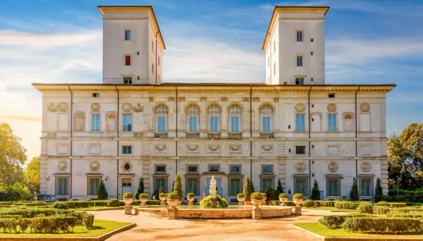 La Villa Borghese à Rome, avec ses tours jumelles et son jardin à la française, sous un ciel bleu éclatant.