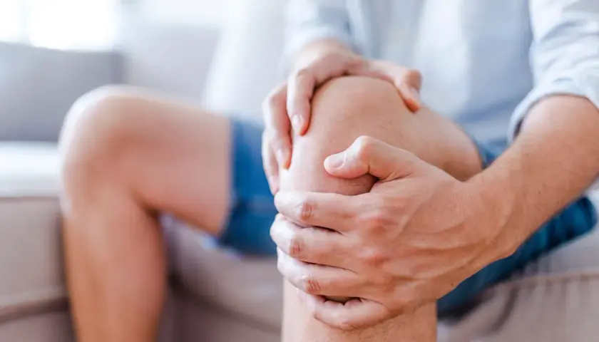 Mężczyzna trzyma się za kolano, odczuwając ból. Kłucie w kolanie utrudnia mu codzienne czynności.