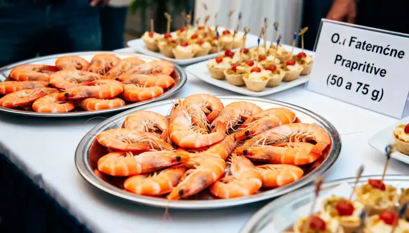 Plateaux de crevettes pour un buffet. Une pancarte indique "O.I Faterne Prapriitive (50 a 75 g)", suggérant combien de crevettes par personne.