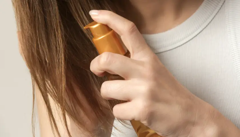 Delikatne olejowanie włosów rozjaśnianych złotym serum. Dłoń aplikuje produkt na brązowe pasma, przywracając im blask i nawilżenie.