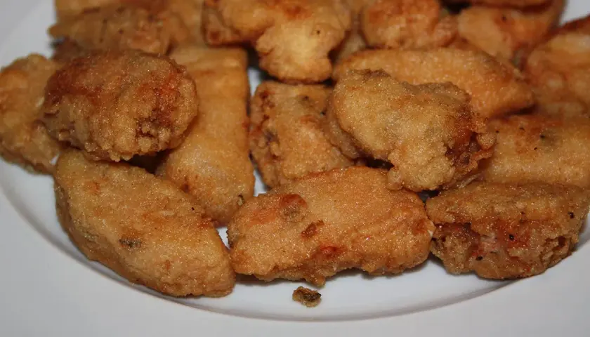 Un plato blanco lleno de trozos dorados y crujientes de japuta en adobo, listos para disfrutar.