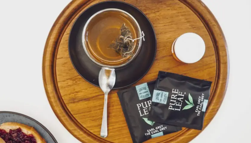 Aromatyczna, najlepsza czarna herbata Earl Grey z Sri Lanki, zaparzona w szklance, obok saszetki i łyżeczka.