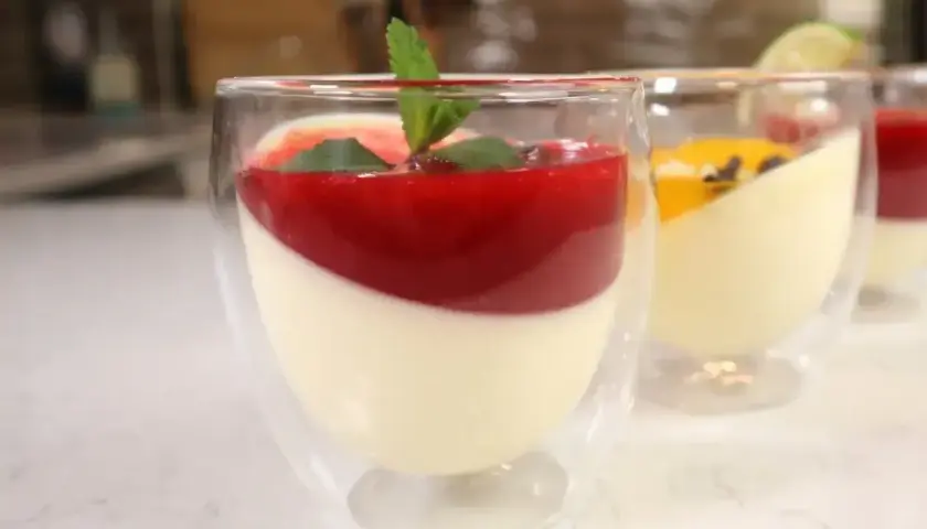 Panna cotta w szklankach z musem malinowym i miętą. Obok deser z musem mango.