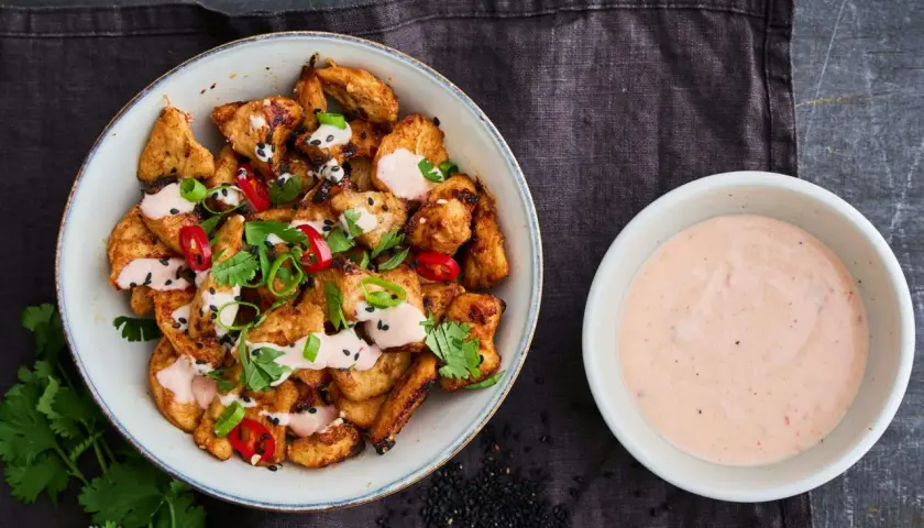 Krispiga kycklingbitar toppade med färska örter, chili och sesamfrön, serverade med en krämig bang bang sås.