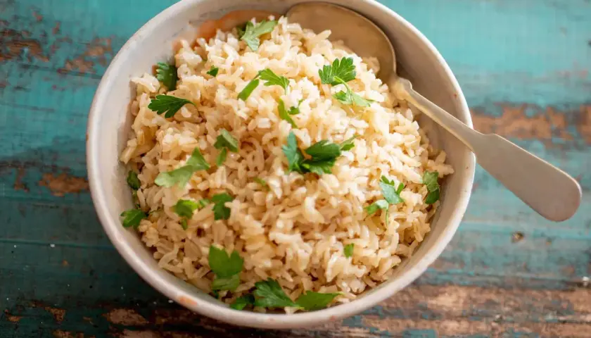 Un tazón de arroz integral esponjoso, perfecto para aprender como hacer arroz integral. Decorado con perejil fresco y una cuchara lista para servir.