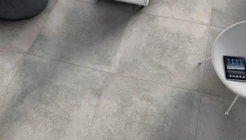 Szare, rektyfikowane płytki tworzą nowoczesną podłogę. Obok wygodny fotel i stolik z książkami.