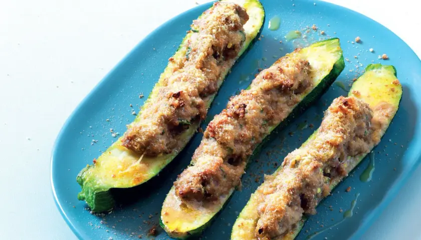 Tre zucchine ripiene velocissime, dorate e appetitose, servite su un piatto blu.