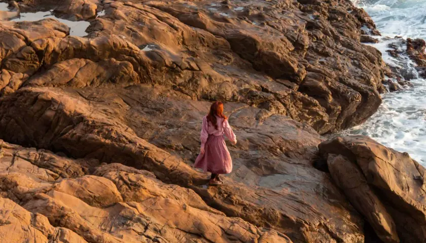Donna con capelli rossi cammina su rocce dorate al tramonto, evocando il significato del golden hour.