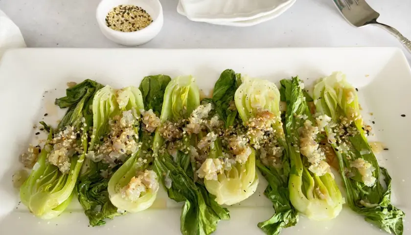 Bok choy tierno salteado con ajo y semillas de sésamo, servido en un plato blanco.