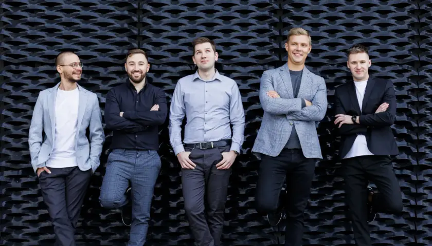 Pięciu mężczyzn w eleganckich strojach, idealnych do sesji fotografia biznesowa, pozuje na tle czarnej, geometrycznej ściany.