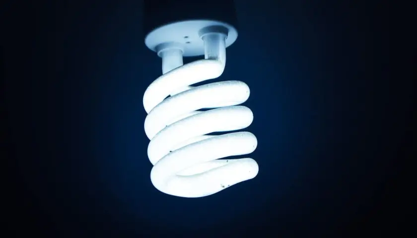 Świeci żarówka energooszczędna, jej spiralne ramiona emanują chłodnym, niebieskawym światłem.