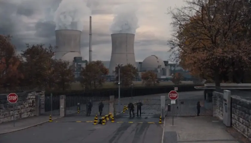 Mroczna elektrownia z chmurami pary nad chłodniami. Strażnicy przy bramie, nie wiadomo, kto jest kim.
