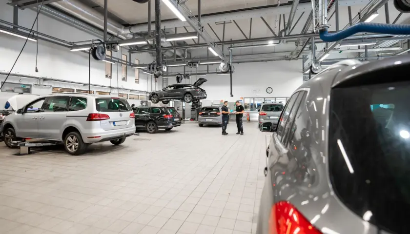 Bilverkstad med flera bilar, en lyft och mekaniker som diskuterar. Dags för volkswagen serviceintervall?