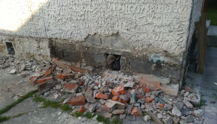 Odkopany fragment ściany z widocznymi uszkodzeniami, gruz i cegły. Rozpoczęcie prac, jak wzmocnić stare fundamenty z kamienia.