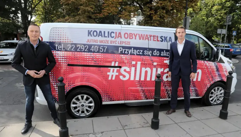 Dwóch mężczyzn stoi obok vana z napisem "Koalicja Obywatelska" i hasłem "#silnirazem".