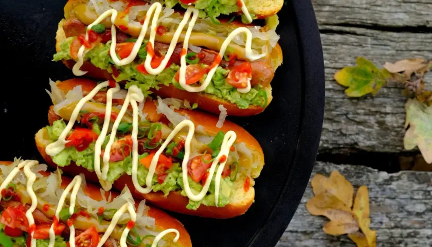 Fyra läckra completos chilenos med avokado, tomat och majonnäs på ett svart fat, redo att avnjutas utomhus bland höstlöven.