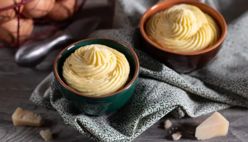 Due ciotole con crema pasticcera salata, guarnita a spirale. In sottofondo uova e formaggio.