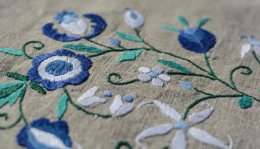 Un fichier broderie aux motifs floraux bleus et blancs sur fond beige. Les détails des points de couture sont visibles.