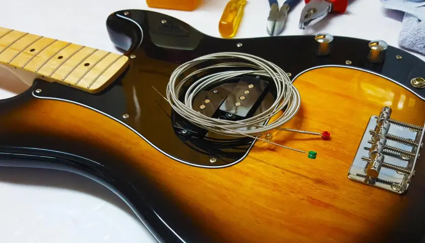 Nowe gitara struny po kolei czekają na założenie. W tle narzędzia do naprawy.