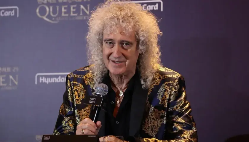 Brian May z zespołu Queen, w ozdobnej marynarce, udziela wywiadu.