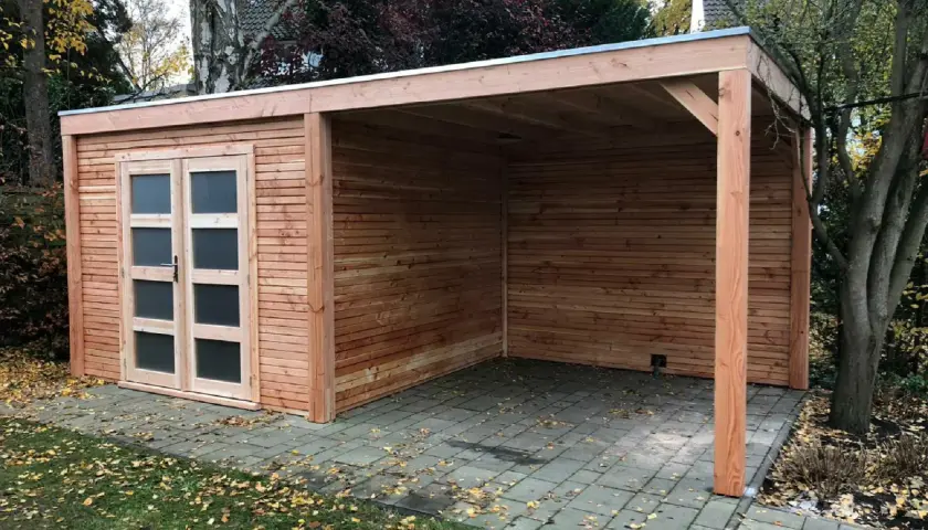Neuer Holzschuppen mit Carport, das Dach ist mit Dachpappe verlegt. Herbstlaub liegt auf dem Boden.
