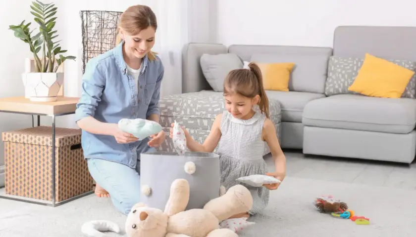 Mama i córka sprzątają zabawki. Dziecko uczy się obowiązków w domu, jakby obowiązywała ustawa o porządku.