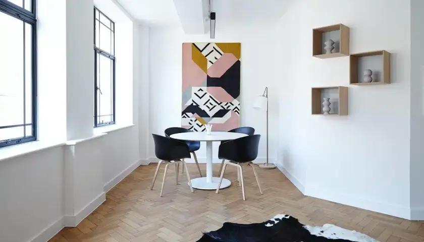 Nowoczesna aranżacja salonu w bloku: okrągły stół z czarnymi krzesłami, geometryczny dywan, lampa i ozdobne półki.