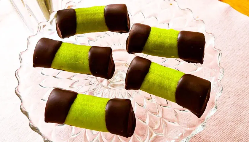 Fem gröna bakelser med chokladtoppar på ett glasfat. Som små dammsugare redo att avnjutas med en kopp kaffe.