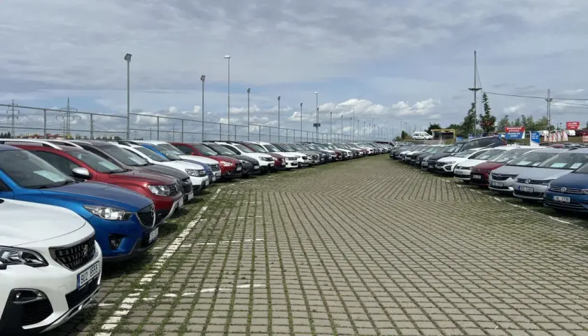 Duży plac z rzędami zaparkowanych samochodów pod zachmurzonym niebem.