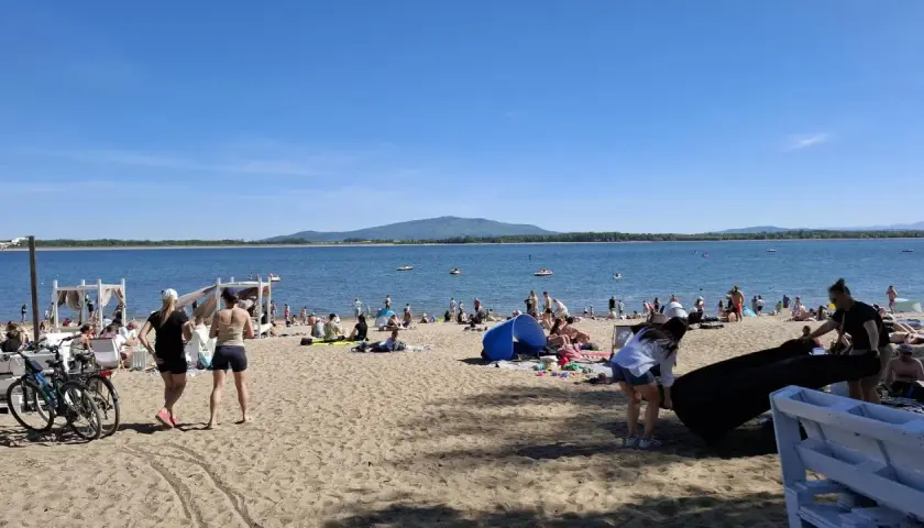 Słoneczny dzień nad jeziorem Mietkowskim. Ludzie odpoczywają na plaży, niektórzy kąpią się w wodzie.