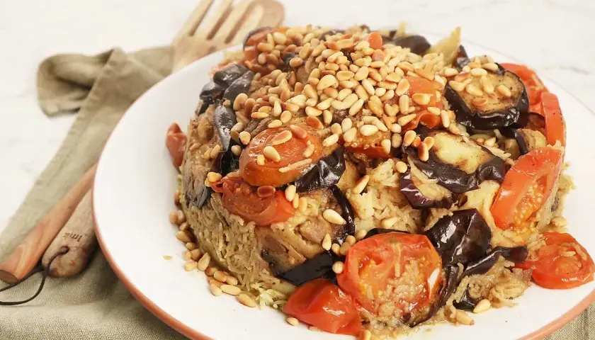 En läcker maklobe kyckling med aubergine, tomater och pinjenötter, serverad på en vit tallrik.