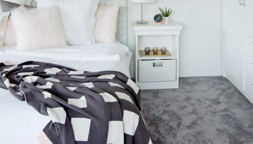 Un letto accogliente con coperta a quadri e un morbido tappeto grigio, perfetto per la posa moquette.