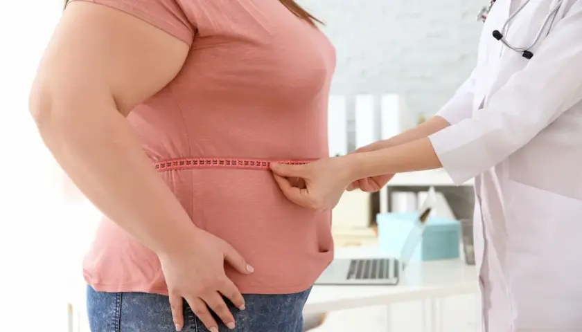 Arzt misst Taille einer übergewichtigen Frau. Mögliche Ursachen für Gewichtszunahme wie Eisenmangel werden besprochen.