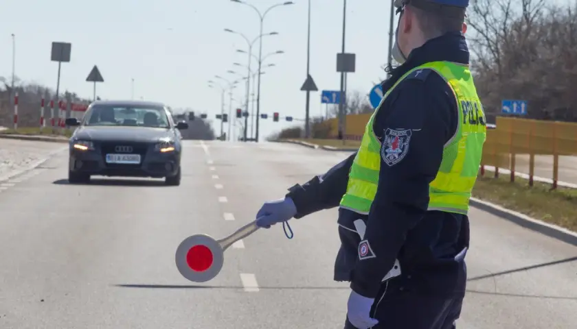 Policjant w kamizelce odblaskowej kieruje ruchem, zatrzymując audi. Nie ma tu fotoradaru, ale kontrola drogowa trwa.