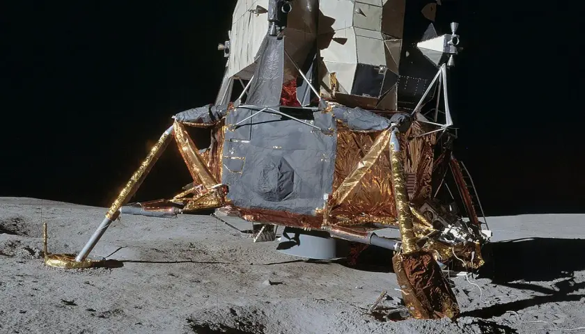 Moduł księżycowy z misji **projekt Apollo** osadzony na szarym gruncie Księżyca.