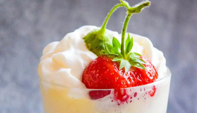 Krem zabaglione z truskawką i bitą śmietaną w szklance.
