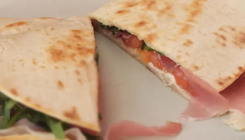 Pyszna piadina romagnola z szynką, pomidorami i rukolą, złożona na pół, gotowa do jedzenia.