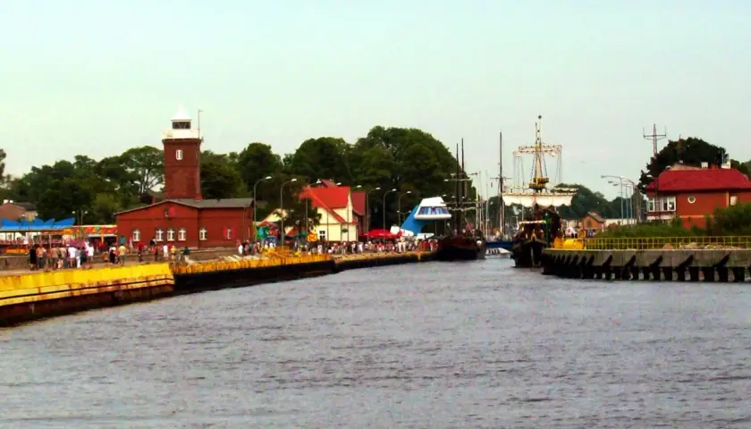 Widok na port z latarnią morską, statkami i ludźmi na nabrzeżu.