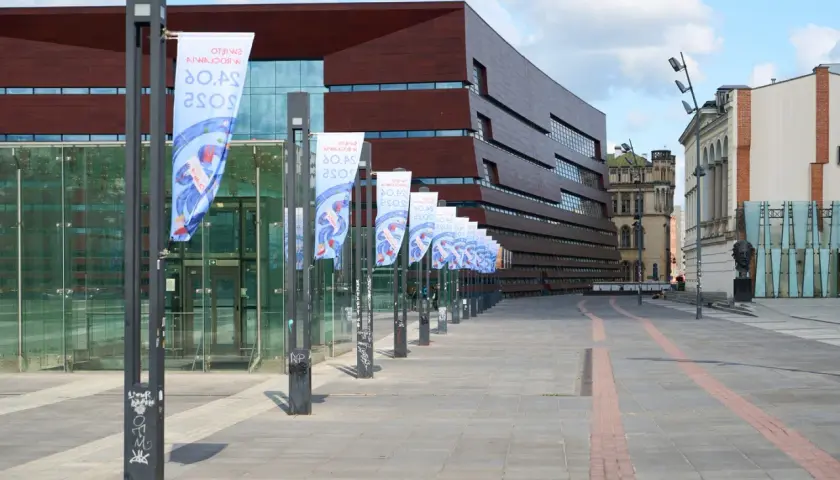 Plac Wolności we Wrocławiu z nowoczesnym budynkiem i rzędem flag.