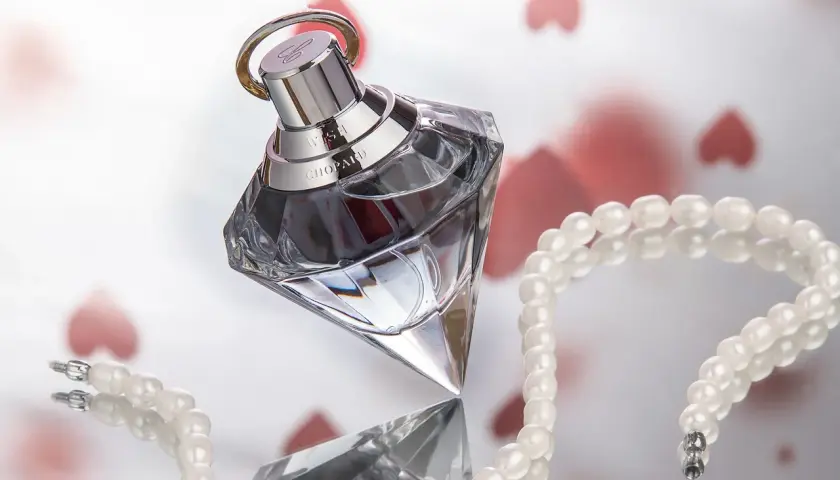 Luksusowy flakon ambperfumy Chopard Wish, otoczony perłami i serduszkami, symbolizuje elegancję i romantyzm.