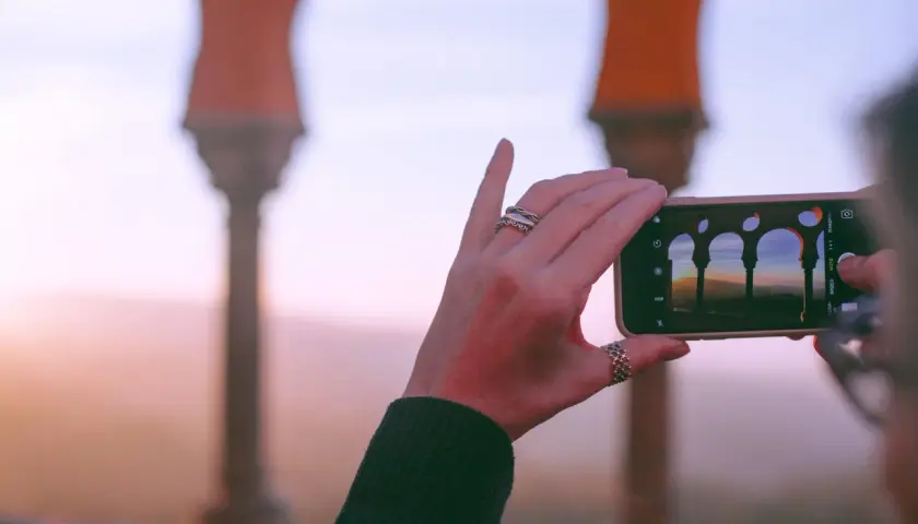 Dłoń z pierścionkami robi zdjęcie telefonu z widokiem na łuki i krajobraz. Międzynarodowy roaming pozwala dzielić się tymi chwilami.