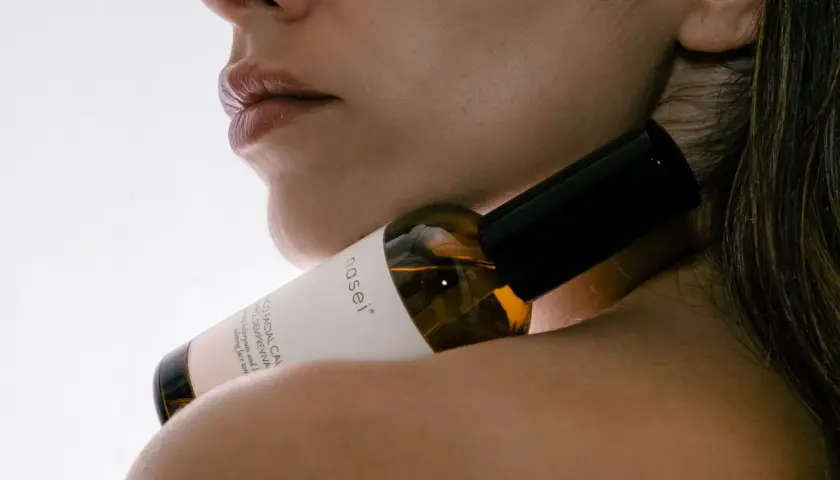 Labios y cuello de mujer con un frasco de sérum facial que contiene ácido hialurónico, para una piel radiante.