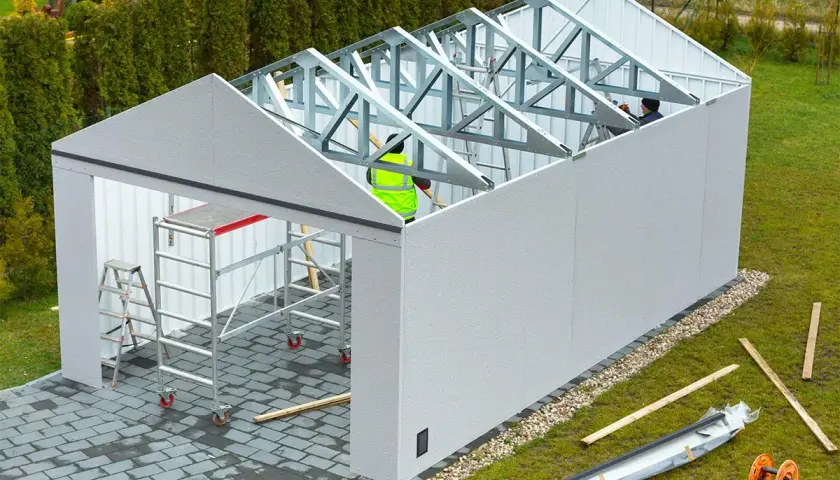 Budowa garażu w toku. Pracownicy montują konstrukcję dachu. Bez zgłoszenia taka budowa może skutkować karą za postawienie blaszaka bez zgłoszenia.