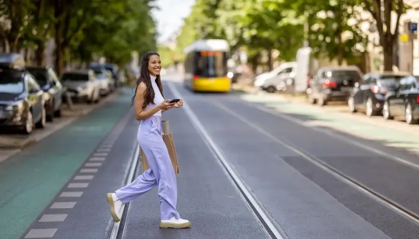 Mujer sonriente cruza la calle con bolsas, disfrutando de su estilo de slow fashion.