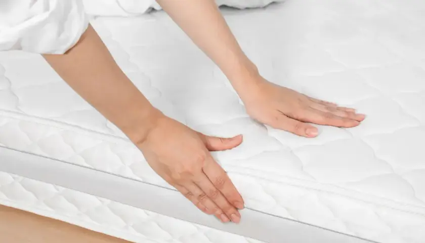 Mains palpant un matelas blanc, peut-être pour évaluer les symptômes d'un matelas trop ferme.