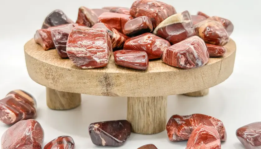 Rote und braune Jaspissteine, die die Bedeutung von Kraft und Vitalität symbolisieren, liegen auf einem Holzpodest und drumherum.