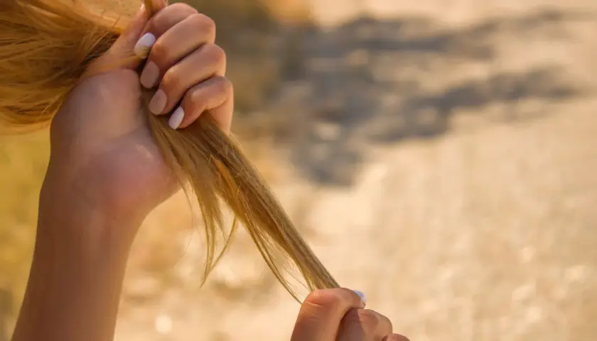 Manos rubias sujetan mechones de pelo, buscando cómo recuperar el pelo quemado.