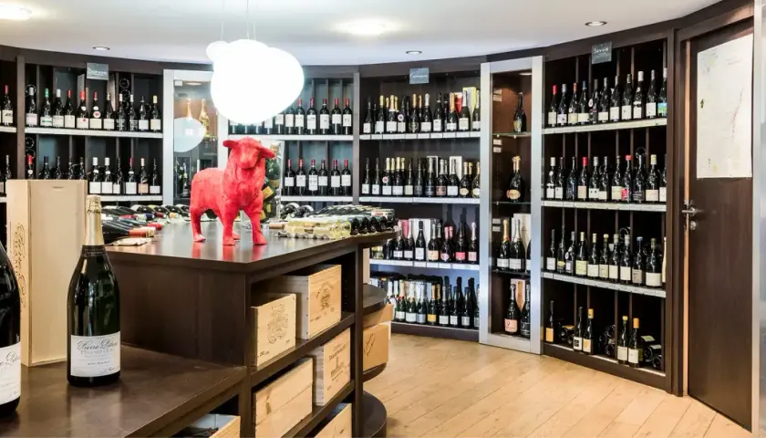 Une cave à vin bien garnie, avec une statue de taureau rouge au centre. Des bouteilles de champagne et de vin sont exposées sur des étagères.